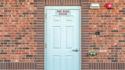 Panorama Fire Riser Room sign on the white wood door of a building with red brick wall