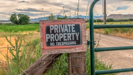 Panorama No Trespassing sign on the wire fence and green metal gate of private property