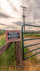 Vertical frame Security gate and fence with No Trespassing sign against mountain and cloudy sky