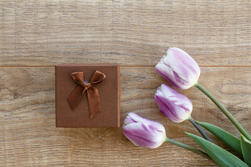 Gift box with tulip flowers on the wooden background.