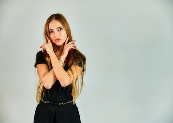 The model stands in different poses in front of the camera. The concept of fashion and style. Portrait of a pretty blonde girl with long hair and great makeup on a white background.