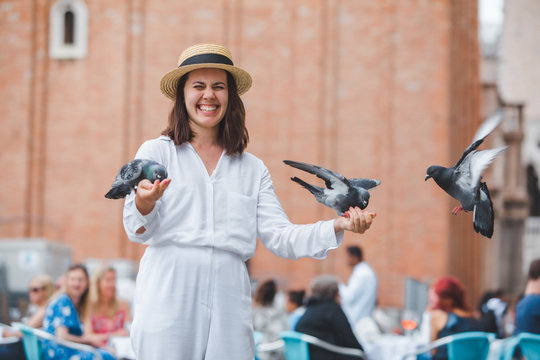 woman in white clothes with straw hat having fun with pigeons at venice city square