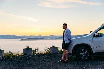 man looking at sunrise in mountains suv car near it