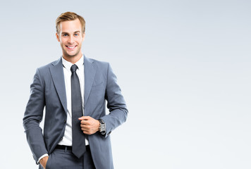 Portrait of happy smiling young businessman in confident suit, on grey background. Business success...