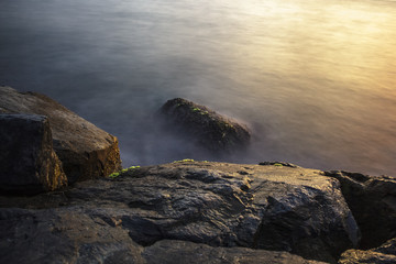 Big boulders sticking out from smooth wavy sea. Romantic atmosphere in peaceful morning at sea. Long exposure shot.