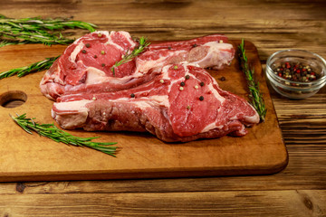 Raw fresh beef rib eye steaks on bone with spices and rosemary on wooden table