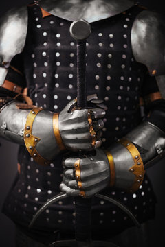 Hands of a medieval knight with a two-handed sword. Warrior holds a sword in his armor.