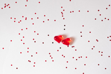 Two red glass hearts on a white background with confetti. The background of Valentine's day