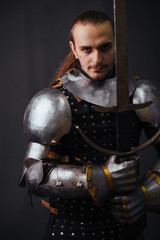 Portrait of a medieval knight with a two-handed sword. Warrior in the studio on a dark background.
