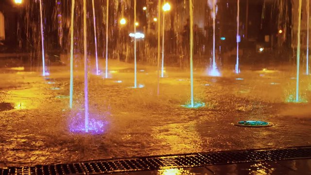 Splashes of fountain. Slow motion of water illuminated in colorful falling on fountain which change it water color in night. Wonderful multicolored fountain throws up high streams of sparkling water.