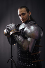 Portrait of a medieval knight with a two-handed sword. Warrior in the studio on a dark background.