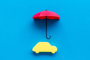 Car protection concept. Automobile cutout defended by umbrella on blue background top-down copy...
