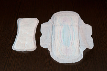 Small and large feminine sanitary pads lie next to a dark background