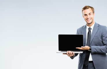 Happy smiling businessman in grey confident suit, showing blank laptop monitor, with copy space for...