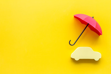 Car protection concept. Automobile cutout defended by umbrella on yellow background top-down copy space