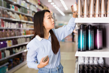 Portrait of young Asian woman choosing hair balm in supermarket