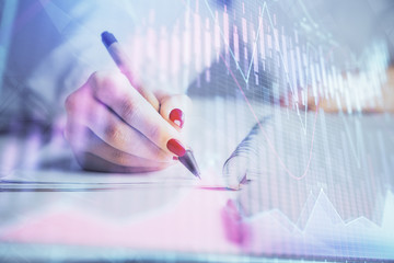 Double exposure of woman's hands making notes with forex graph hologram. Concept stock market...