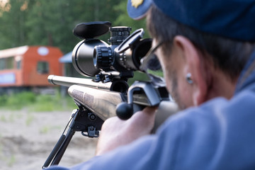 A man with glasses with a beard holds a sniper rifle