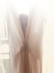 Woman hiding behind the window curtain indoors.