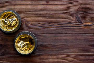Whiskey with ice. To glasses of strong alcohol drink on dark wooden desk top-down frame copy space