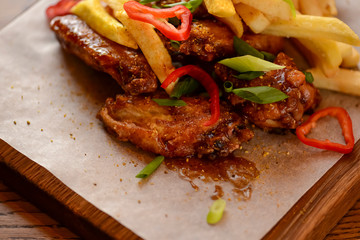 French Fries with fried chicken served with sauce on a wooden cutting board over wooden table background