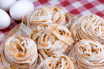 Uncooked fettuccine nest with flour on wooden board Tasty Fresh Colorful Ingredients for Cooking Pasta. Plaid background