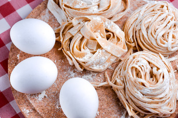 Uncooked fettuccine nest with flour on wooden board Tasty Fresh Colorful Ingredients for Cooking Pasta. Plaid background