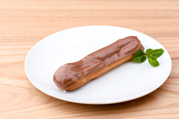 One piece of chocolate cake with vanilla cream and cherry topping served on white plate over light wooden background.