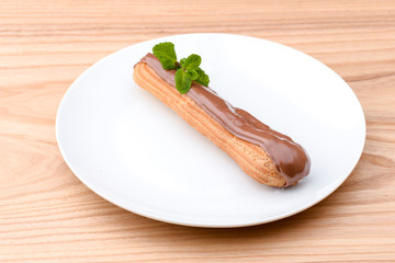 One piece of chocolate cake with vanilla cream and cherry topping served on white plate over light wooden background.