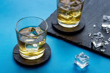 Whiskey near ice cubes on blue background