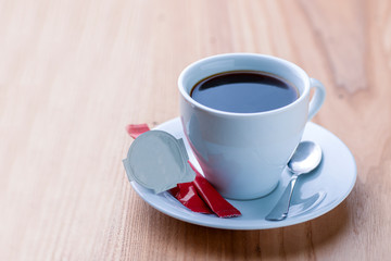Cup of coffee with sugar and cream served on a plate with a spoon on light wooden background.