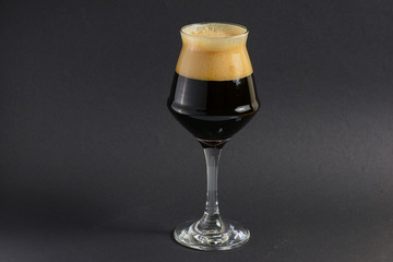 One tall glass of cold dark craft beer over black background. Copy space.