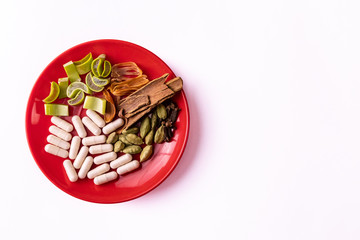 Assorted whole spices with ayurvedic capsules and sliced aloe vera in a plate on white background. Herbal medicines concept