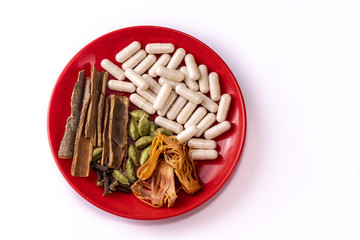 Ayurvedic medicine capsules, cinnamon sticks, cloves, cardamom and mace or javitri in a red dish...