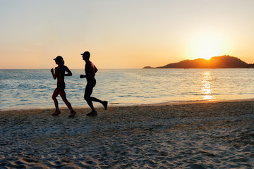 Man and women running on tropical beach at sunset. Healthy lifestyle concept.