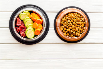 Healthy feed for cats and dogs. Bowls full of dry feed, meat and vegetables on white background top-down copy space