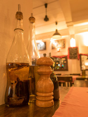 Glass vinegar bottles with a wooden pepper grinder on a restaurant table with warm cosy lighting