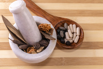 Close-up view of whole spices for grinding in mortar pestle with herbal capsules and tablets in a wooden spoon on a chopping board. Ayurvedic and Unani medicine system concept