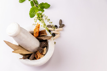 Collection of different spices and herbal tablets with tulsi leaves in white mortar pestle on white...