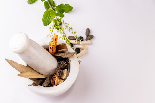 Collection of different spices and herbal tablets with tulsi leaves in white mortar pestle on white background. Herbal and ayurvedic concept