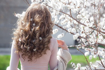 Woman`s hair at spring background. Curly hair. Unrecognizable young woman with flowers in her hair.