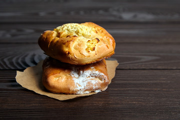 Wheat buns with curd filling on a wooden table, close-up. Bakery, two buns with cottage cheese on baking paper on brown background