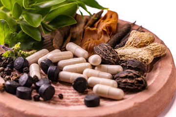 Macro shot of whole unground herbs, spices, pills and capsules on a stone with white background. Ayurvedic medicine concept