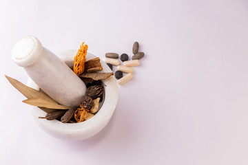 Top view of a mortar & pestle with whole spices to ground and scattered herbal tablets on a white...