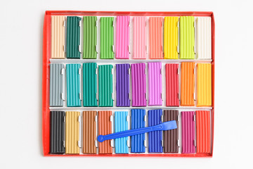Naklejka premium Multi-colored plasticine sticks in a cardboard box. Colorful plastic polymer clay set and sculptural knife on white background.