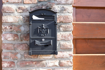 Black mail box with white letter on brick wall with wooden door