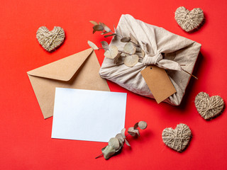 Zero waste Valentine's Day concept and mock up on red. Eco-friendly gift cloth wrapping in Furoshiki style, craft paper envelope,empty greetings card. Top down view or flat lay. Copy space for design