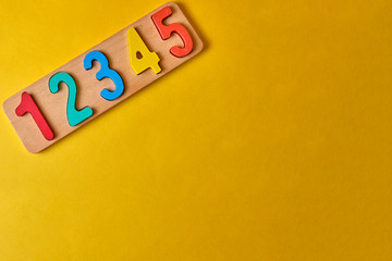 wooden colorful digits and plank at yellow background with copyspace