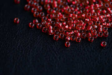 Transparent seed beads red color scattered on a dark background close-up