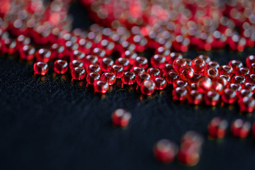 Transparent seed beads red color scattered on a dark background close-up
